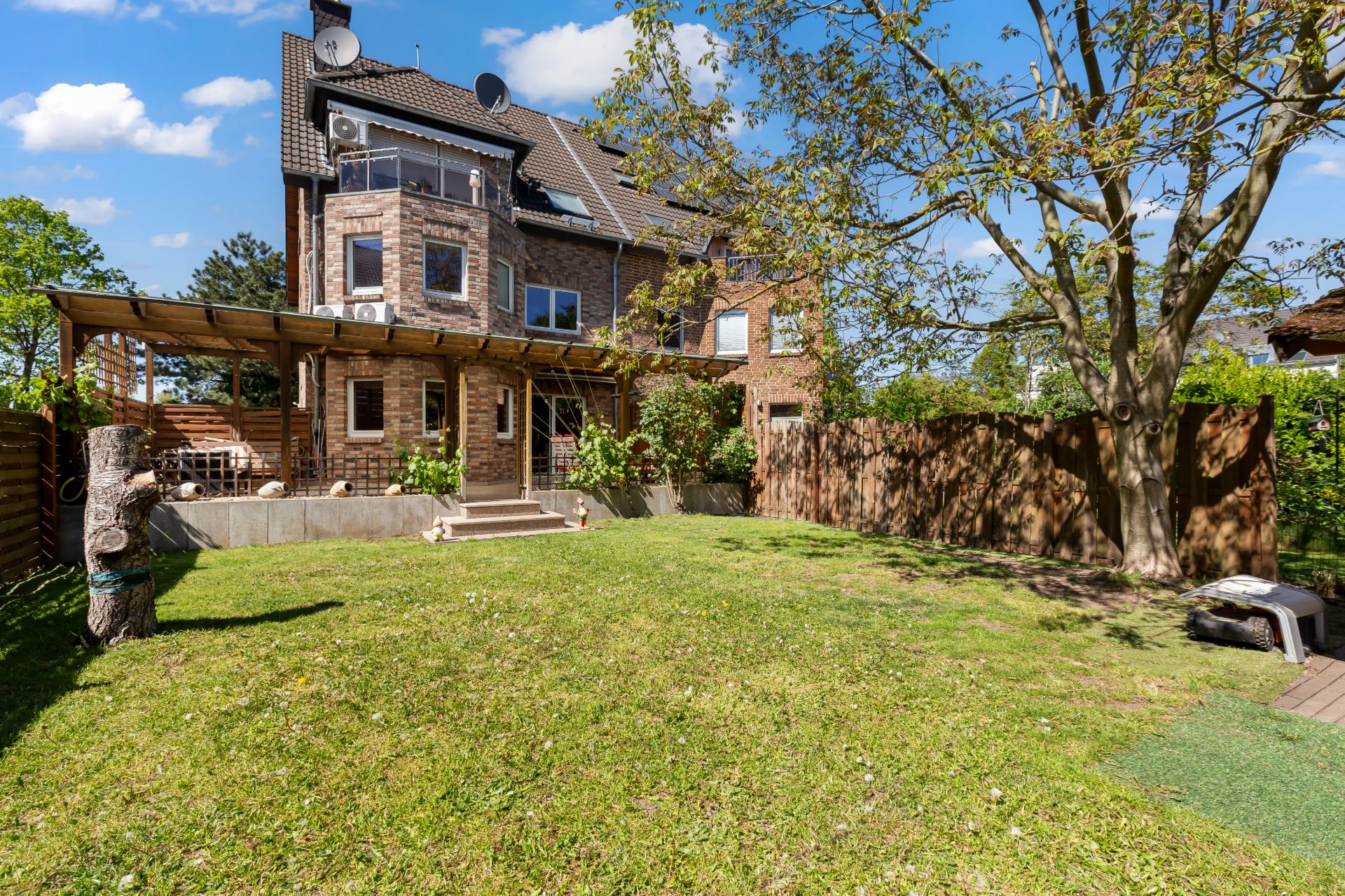Backsteinwohnhaus mit Terrasse und großem Garten, ein Baum steht rechts im Bild.