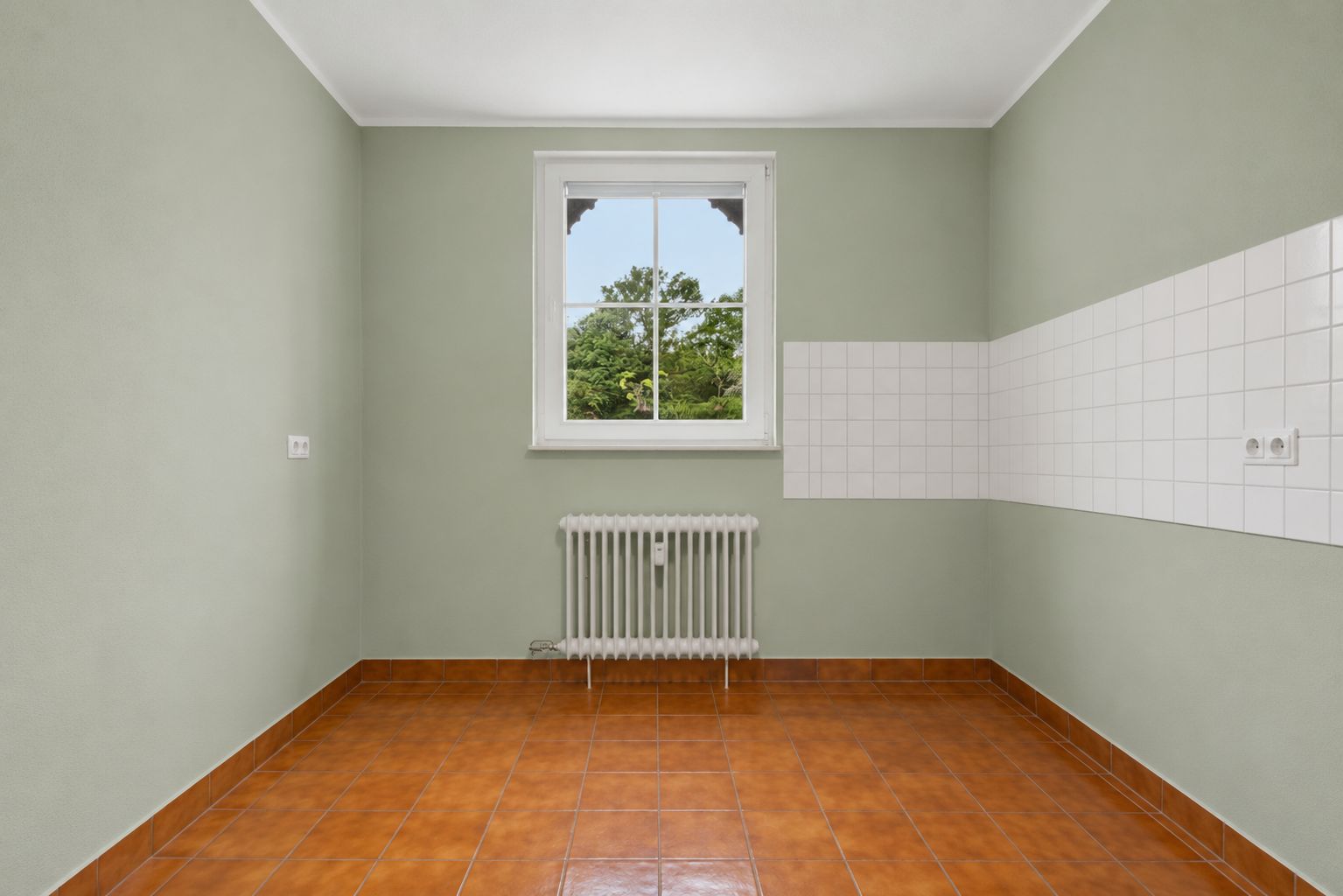 Leerer Raum mit braunen Fliesen, Fenster, Heizkörper und weißen Wandfliesen.