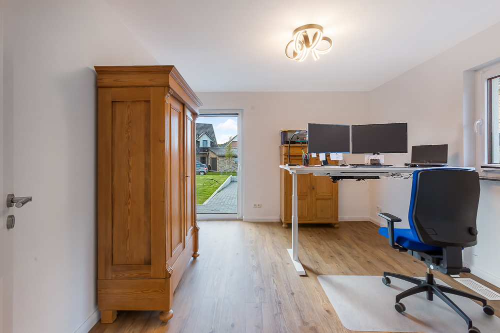 Modernes Arbeitszimmer mit Holzschrank, Schreibtisch mit Monitoren und Schreibtischstuhl auf Holzfußboden.