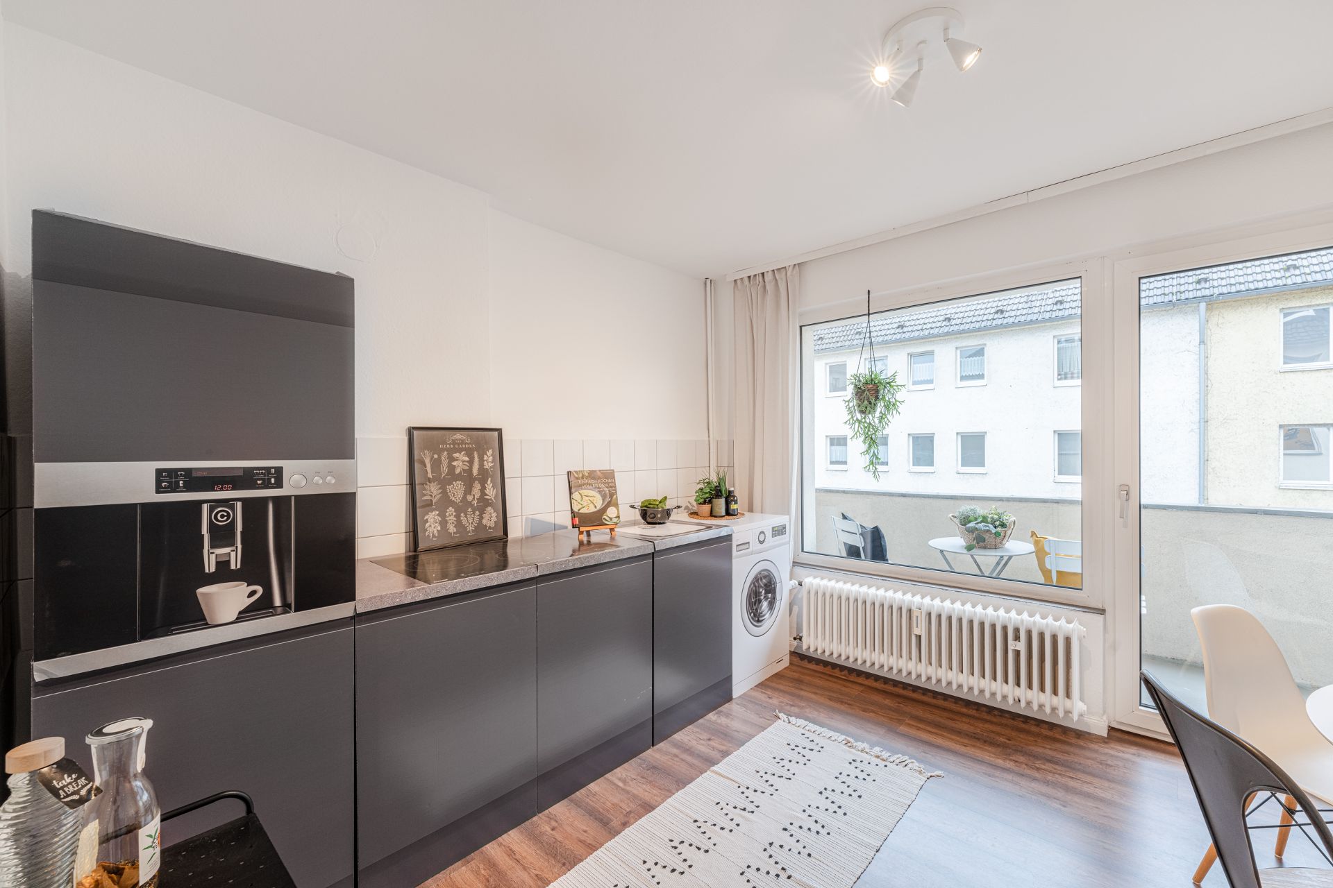 Moderne Küche mit schwarzen Schränken, Kaffeemaschine, Waschmaschine und Zugang zu einem Balkon.