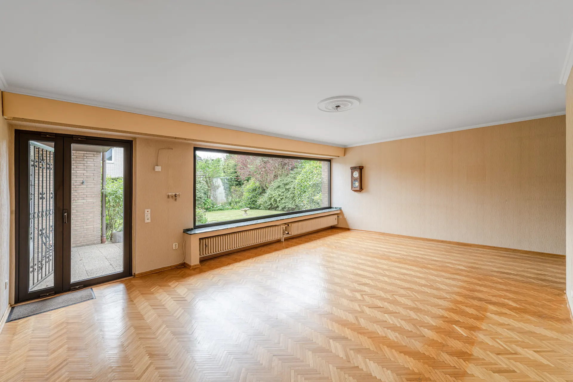 Helles Wohnzimmer mit Parkettboden, großer Fensterfront und Blick in den Garten.