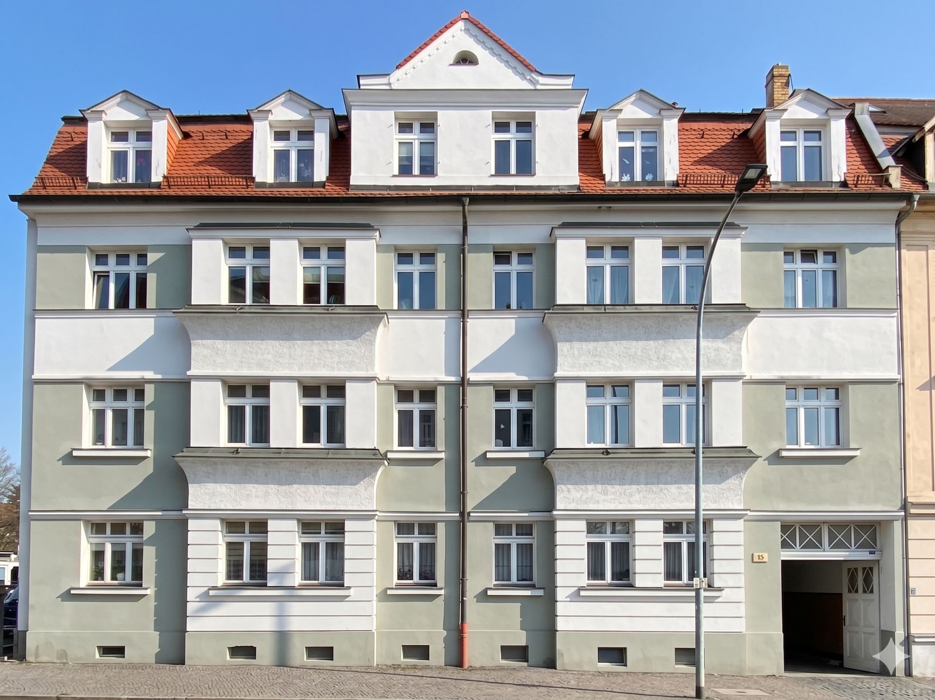 Vierstöckiges Wohnhaus mit weiß-grüner Fassade und rotem Dach, viele Fenster.