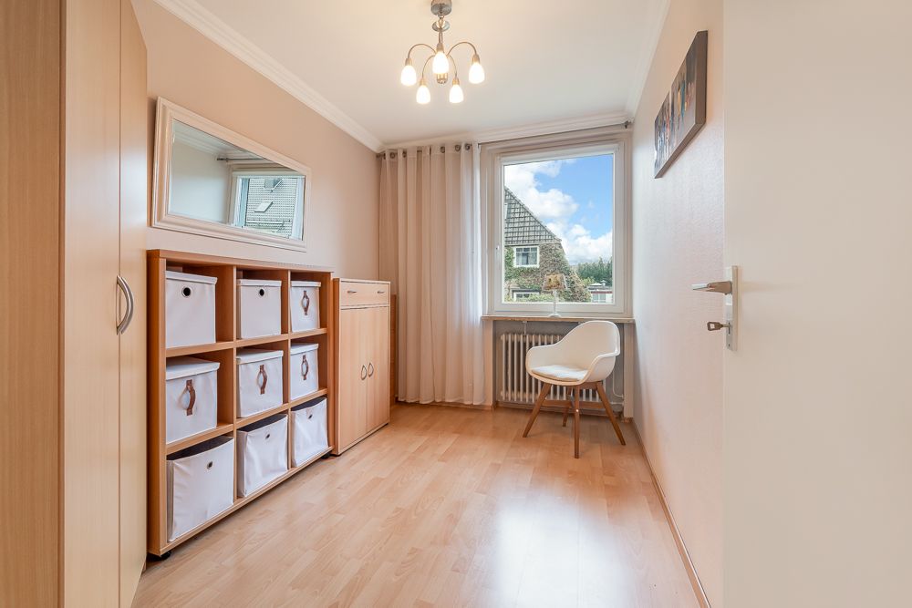 Heller Raum mit Holzschrank, Regalen mit Boxen, Stuhl und Fenster mit Blick nach draußen.