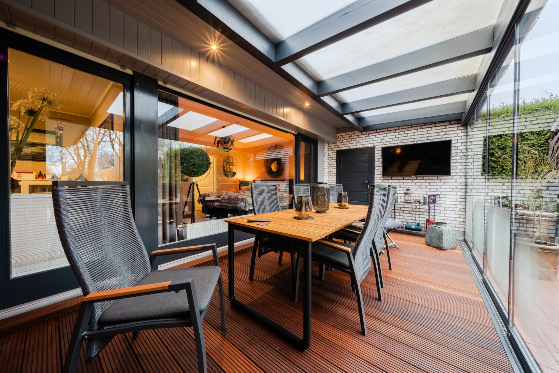 Überdachte Terrasse mit Holzboden, Esstisch, Stühlen und Glastüren, Blick ins Wohnzimmer.