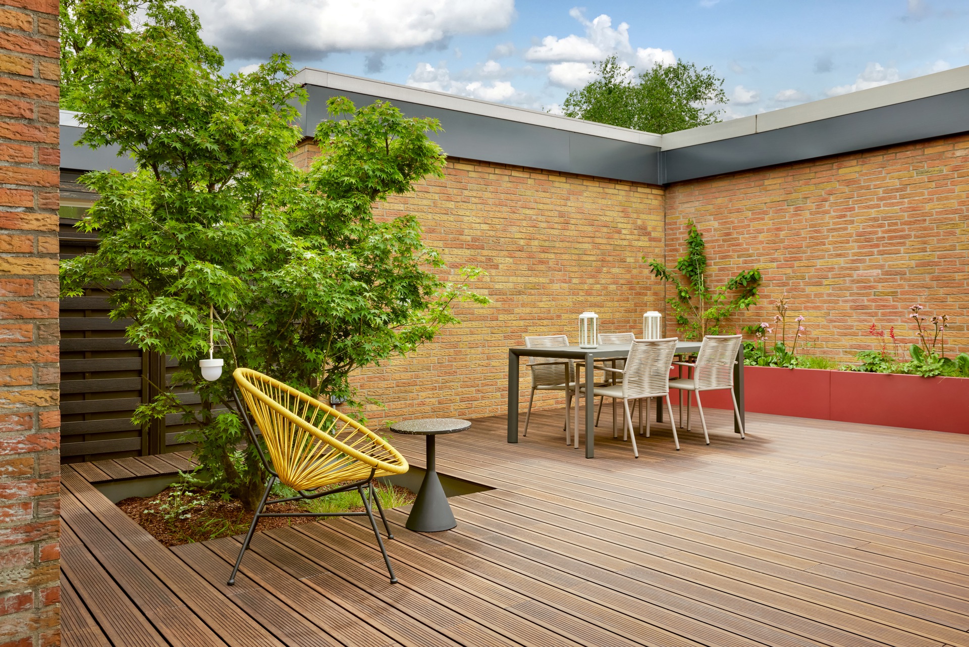 Holzterrasse mit gelbem Stuhl, Esstisch und Baum, umgeben von Backsteinmauern.