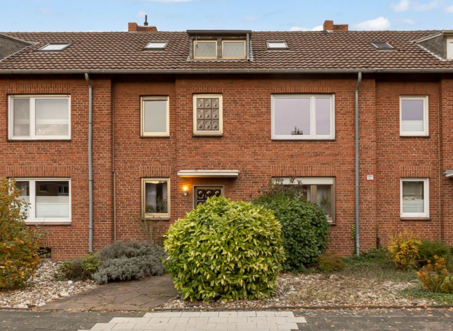 Reihenhaus aus rotem Backstein mit Vorgarten und großen Fenstern.