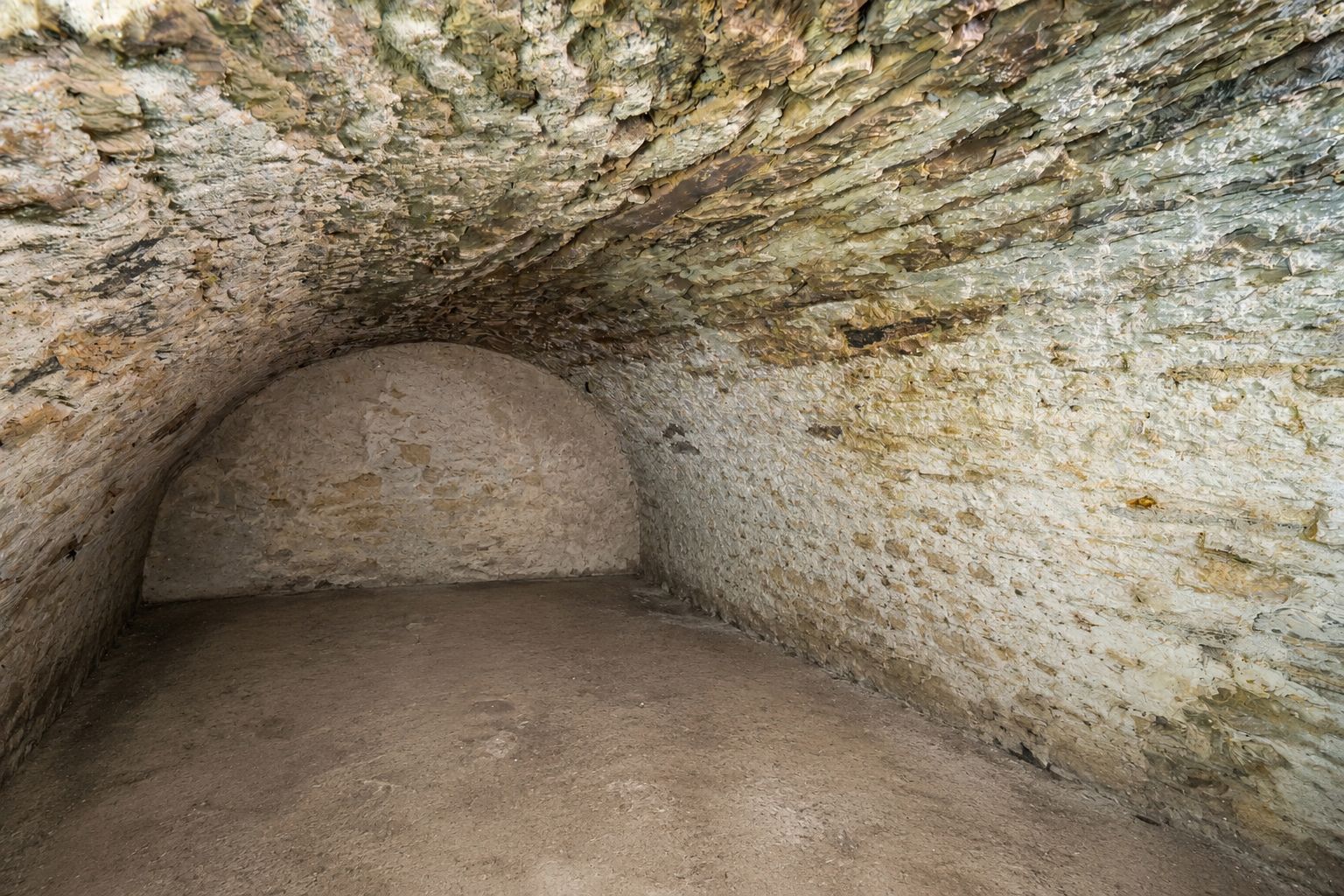 Leerer Kellerraum mit gewölbter Decke und Wänden aus Naturstein.