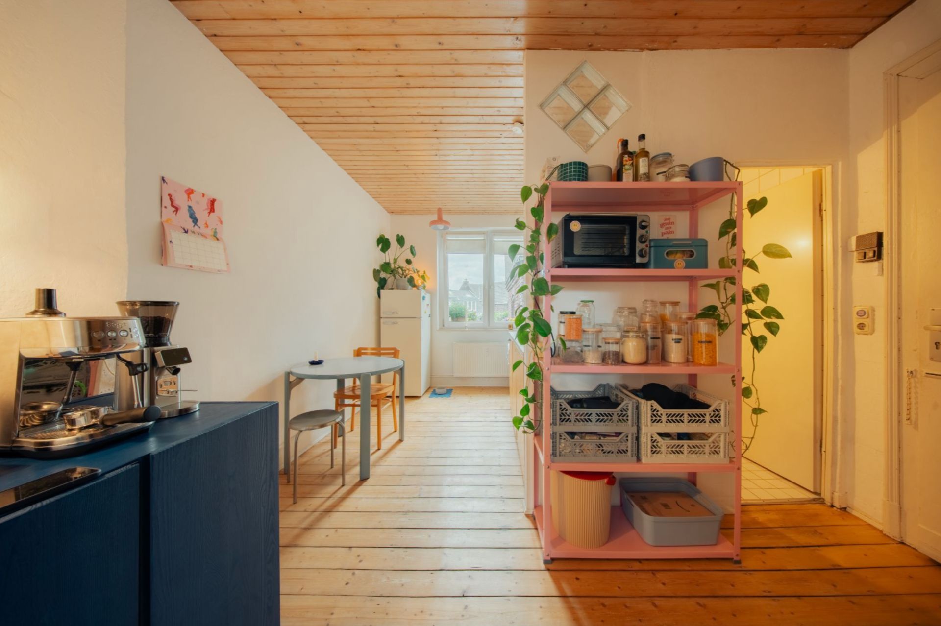Helle Küche mit Holzdecke, blauem Schrank, offenem Regal und Esstisch an der Wand.