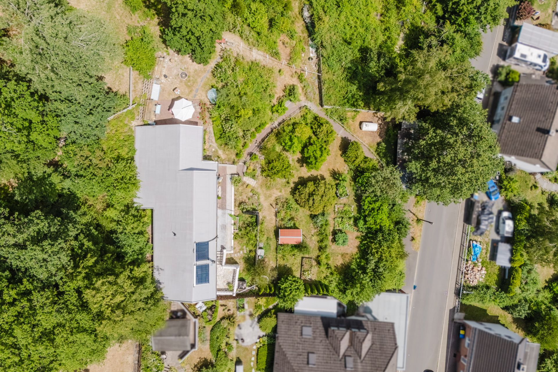 Luftaufnahme eines Hauses mit Garten, Wegen und umliegenden Bäumen in einem Wohngebiet.