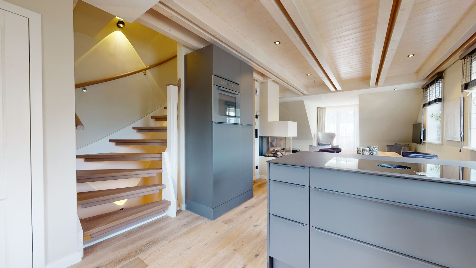 Helle Wohnküche mit Holztreppe, modernen grauen Schränken und großen Fenstern.