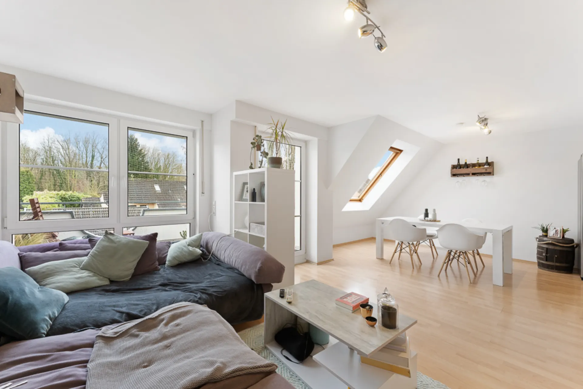 Helles Wohnzimmer mit Sofa, Esstisch und großen Fenstern mit Blick ins Grüne.