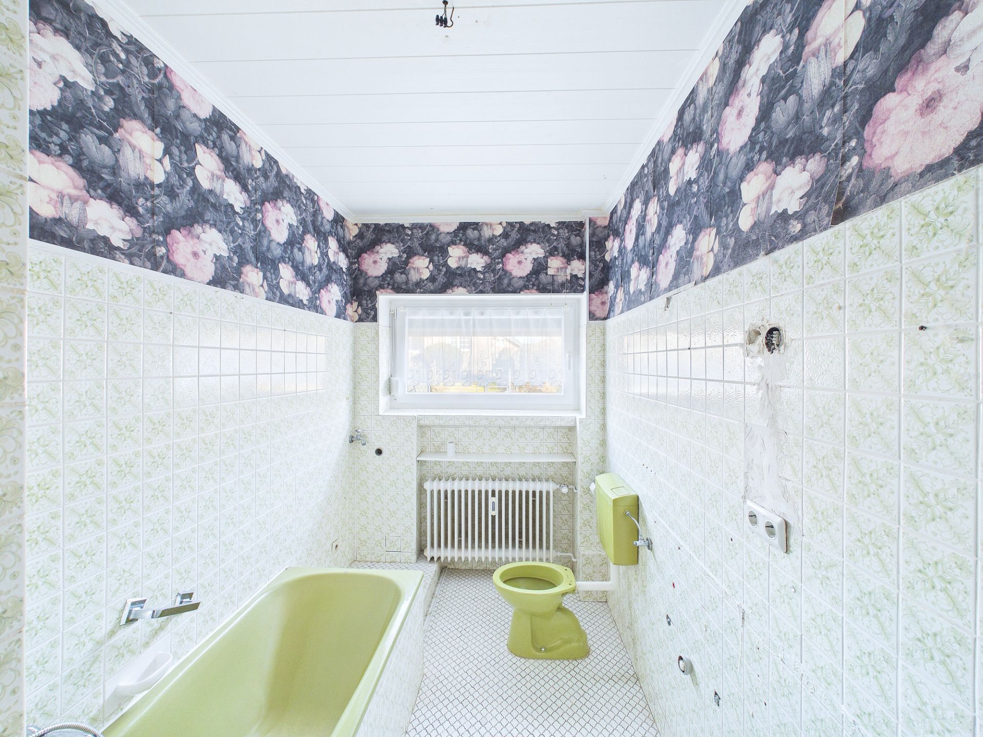 Badezimmer mit grüner Badewanne, Toilette, gemusterter Tapete und Fenster.