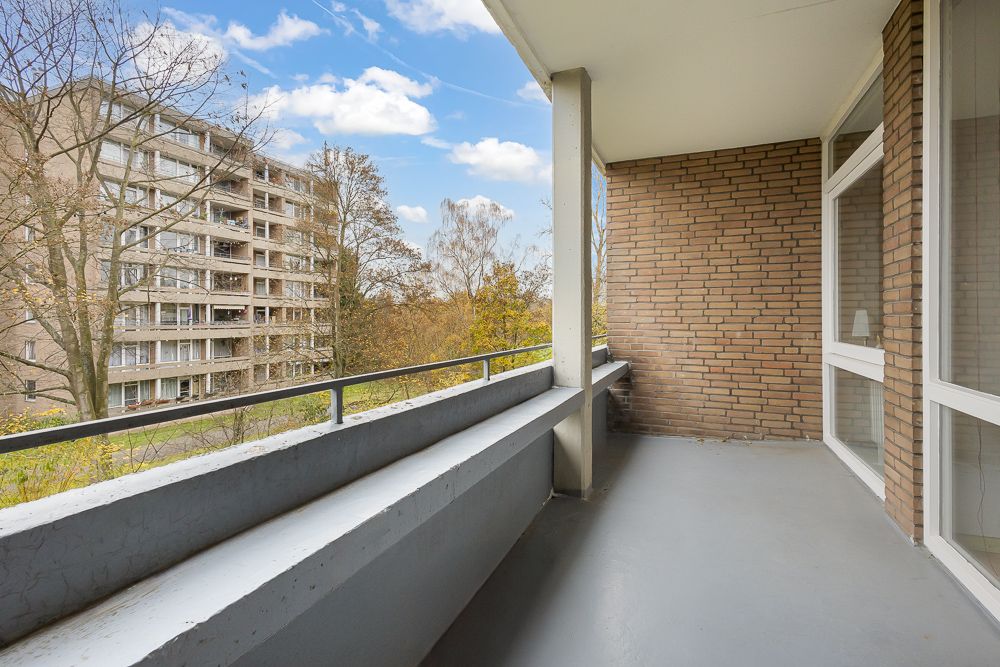 Balkon mit grauem Boden und Backsteinwand, Ausblick auf Wohngebäude und Bäume.
