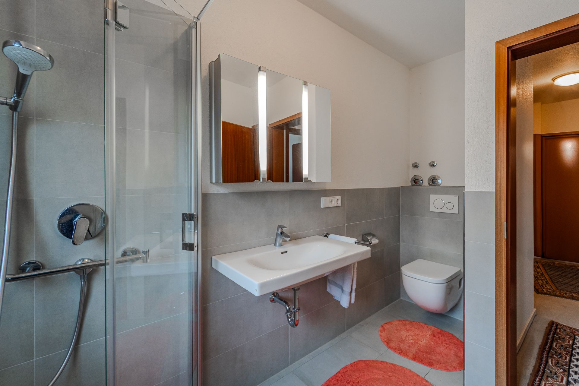 Modernes Badezimmer mit Dusche, Waschbecken, Spiegel, Toilette und roten Teppichen.