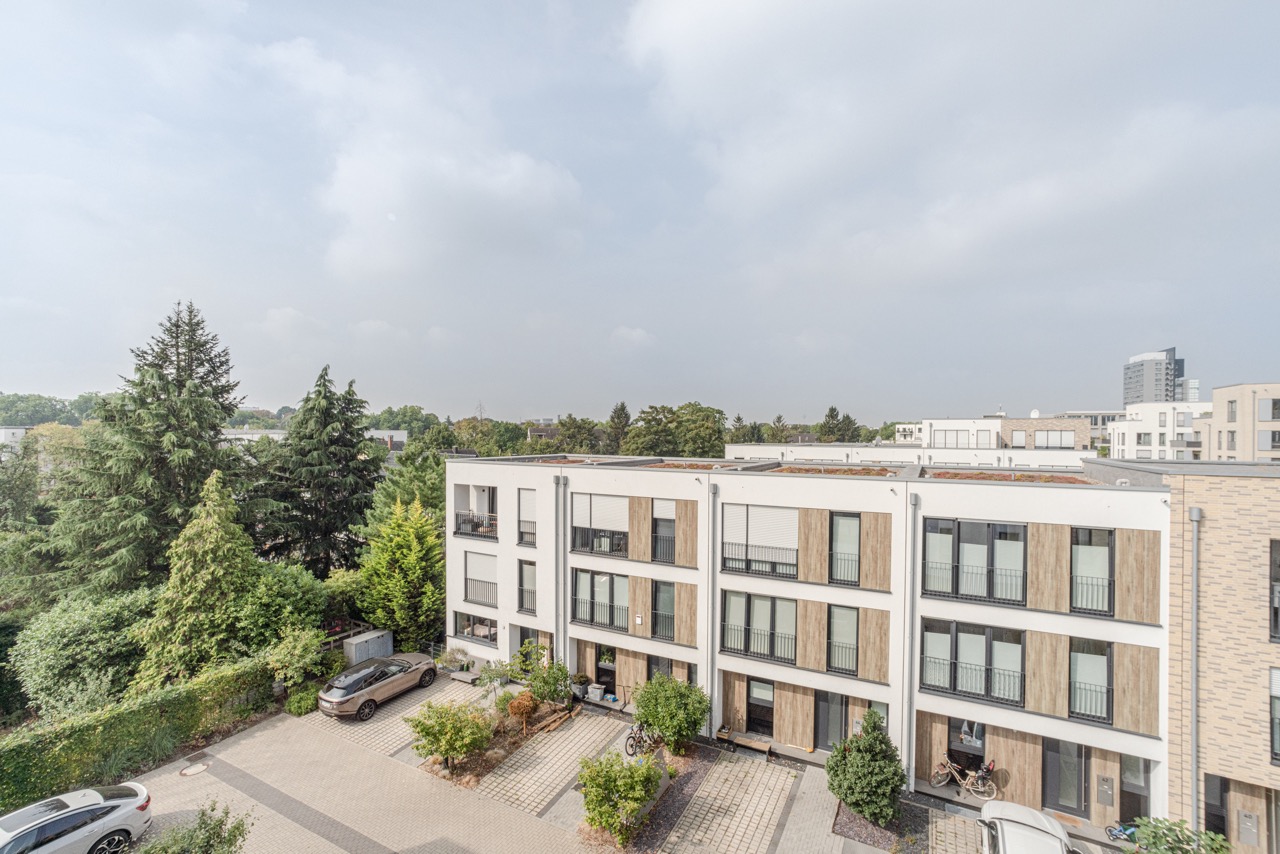 Moderne Wohngebäude mit drei Etagen, davor geparkte Autos und viel Grün.