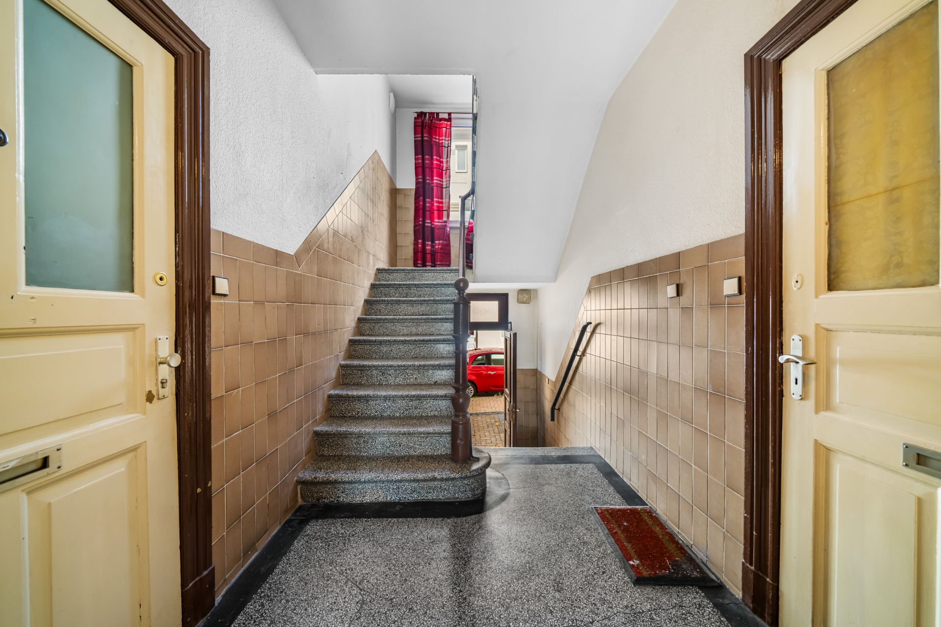 Treppenhaus mit zwei gelben Türen, braunen Fliesenwänden und Stufen nach oben.
