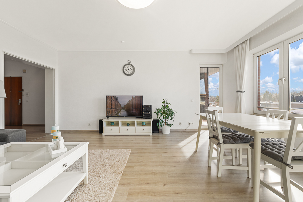 Helles Wohnzimmer mit Holzboden, Esstisch, großen Fenstern, TV und Pflanze.