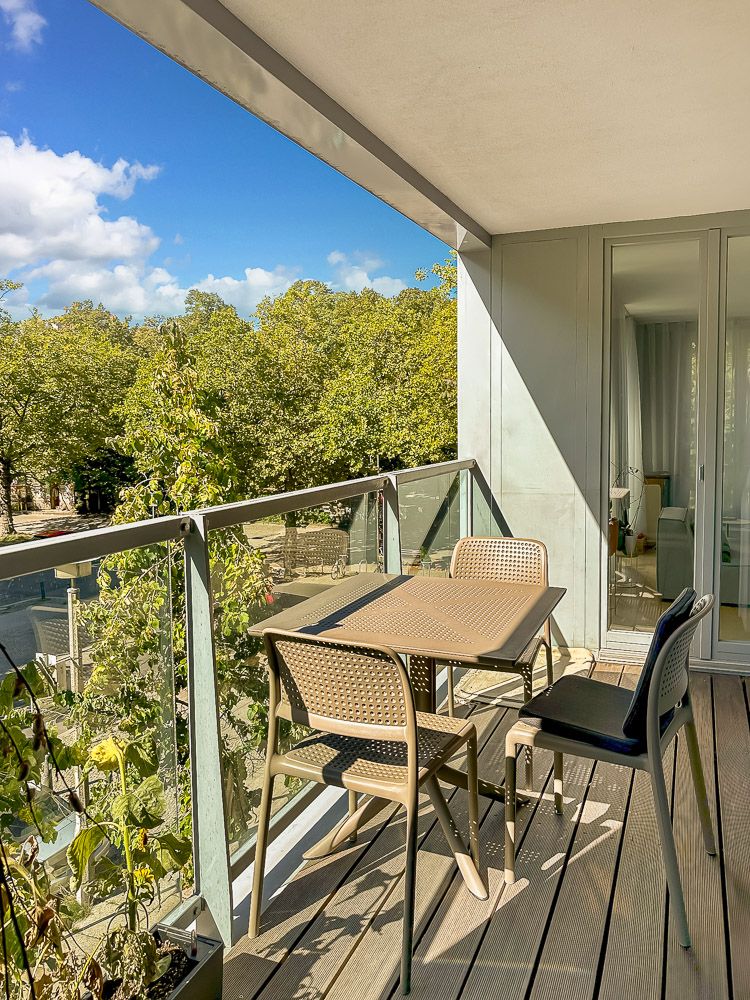 Moderner Balkon mit Tisch und vier Stühlen, Blick auf Bäume und blauen Himmel.