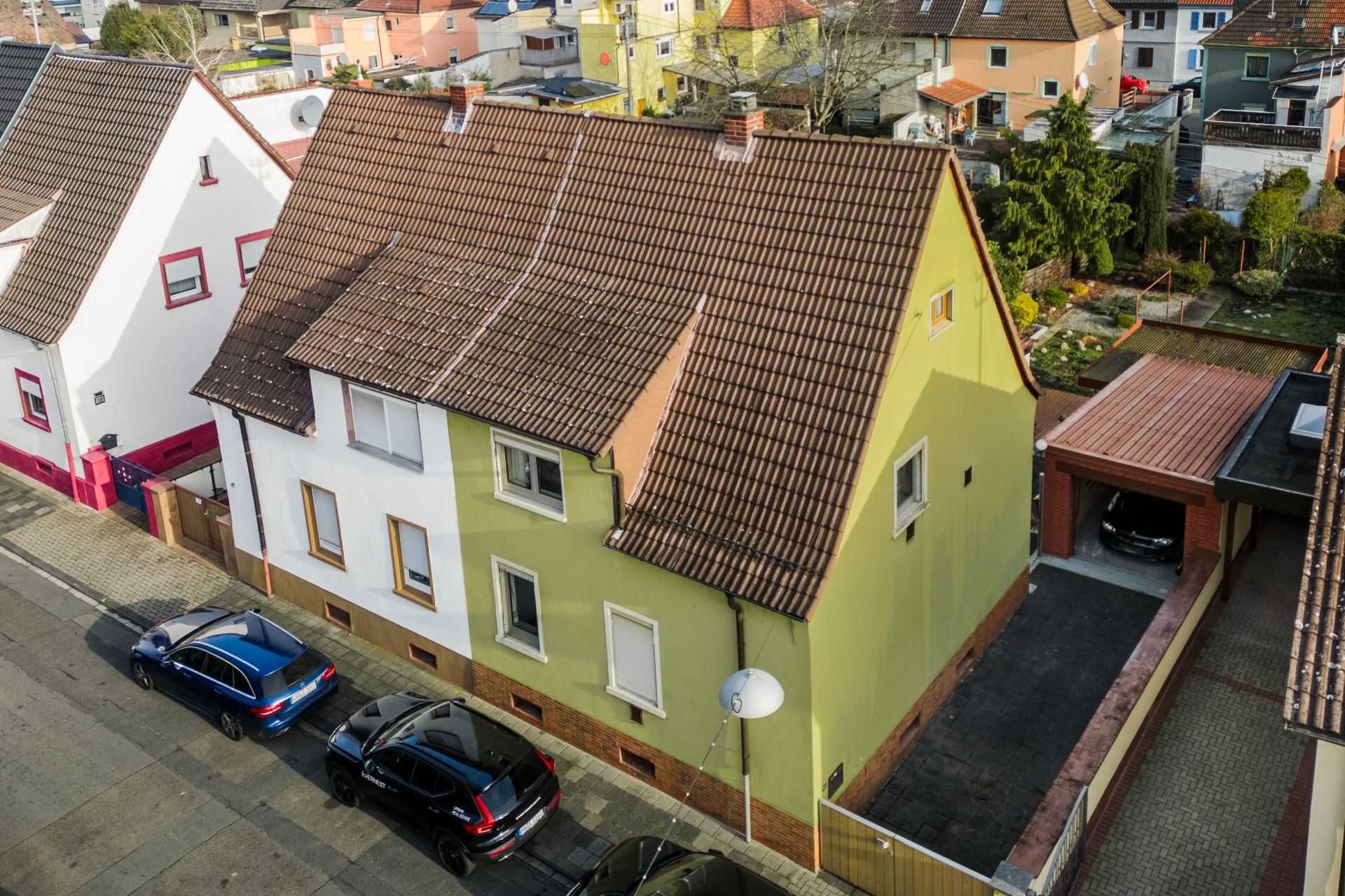 Wohnhaus mit grün-weißer Fassade, schrägem Dach, Einfahrt und geparkten Autos davor.