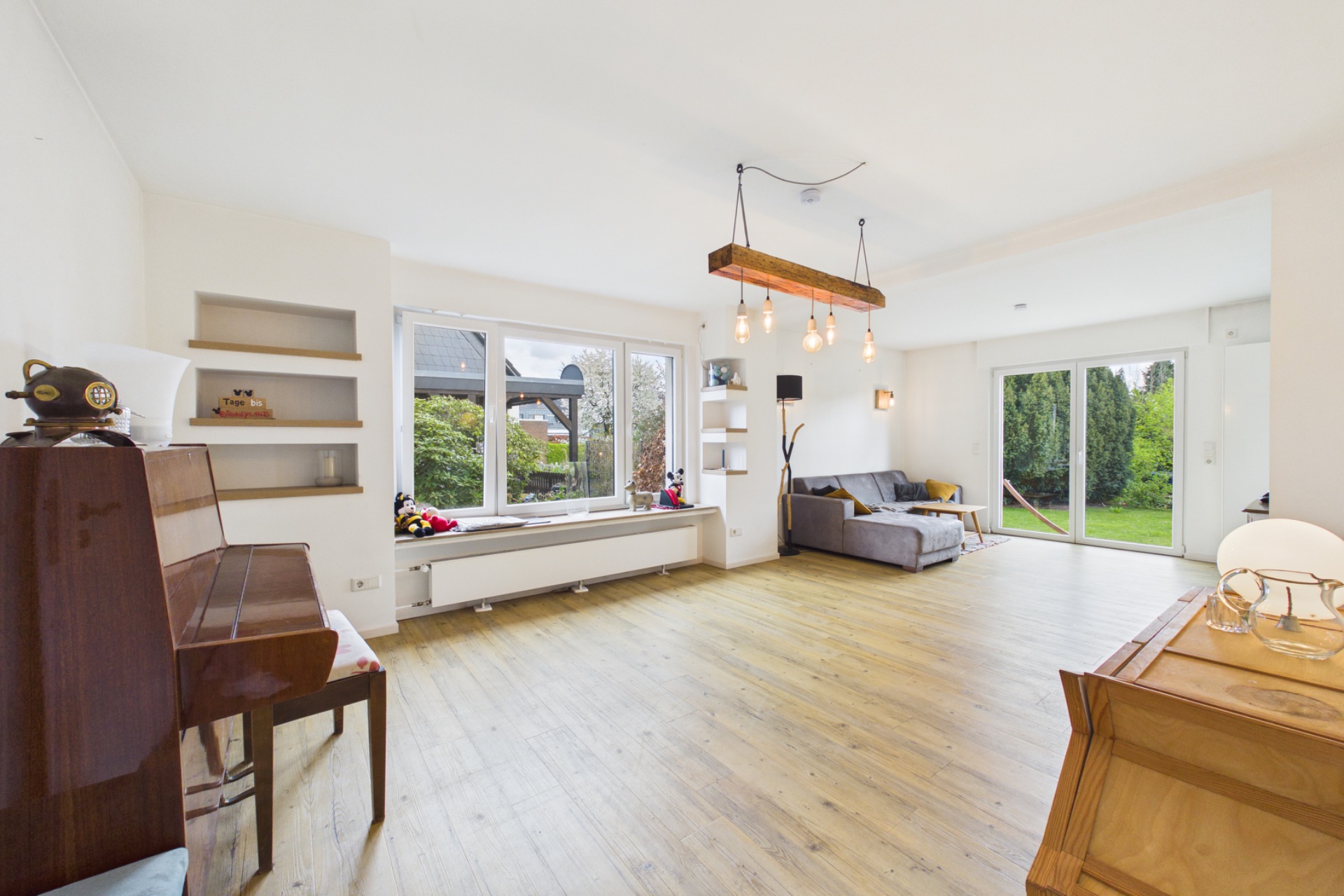 Helles Wohnzimmer mit Klavier, Sofa, großen Fenstern und Zugang zum Garten.