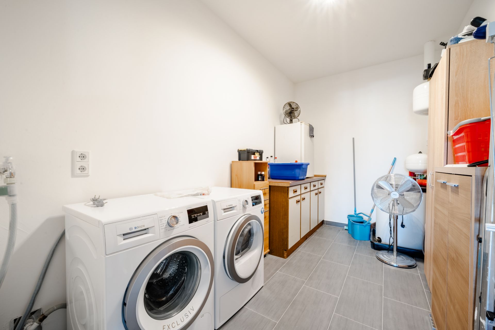Hauswirtschaftsraum mit Waschmaschine, Trockner, Schränken und Ventilator.
