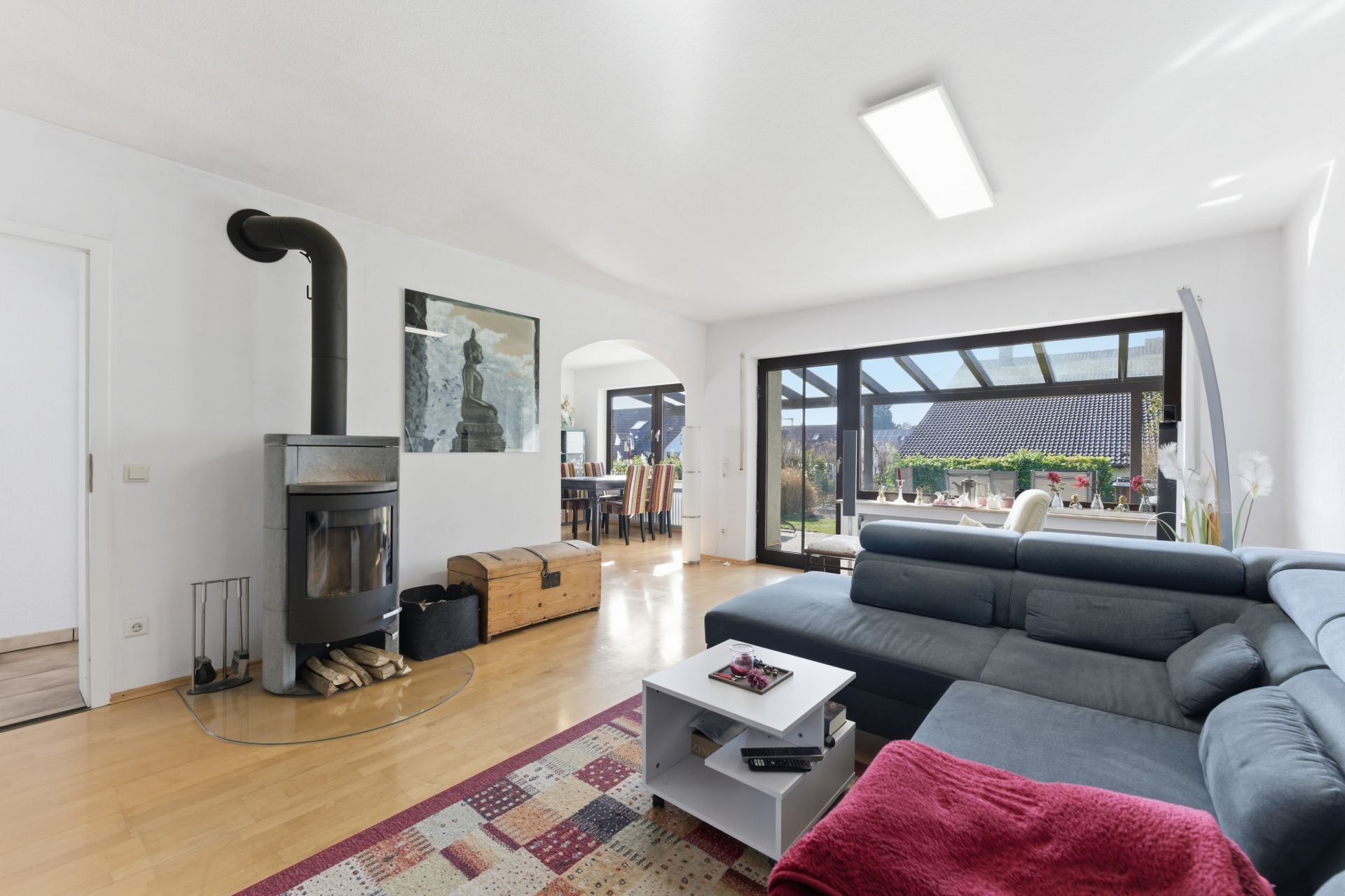 Helles Wohnzimmer mit Kaminofen, Ecksofa, Couchtisch und Zugang zur Terrasse.