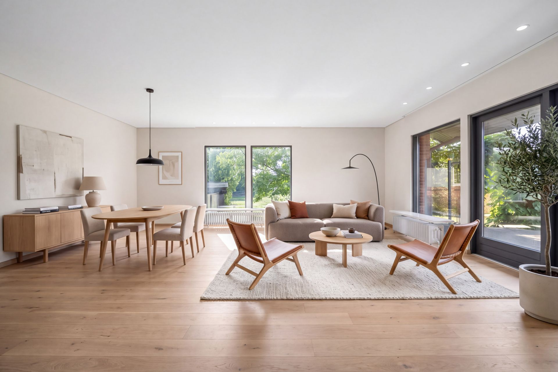 Modernes Wohnzimmer mit Sofa, zwei Sesseln, Esstisch und großen Fenstern zum Garten.
