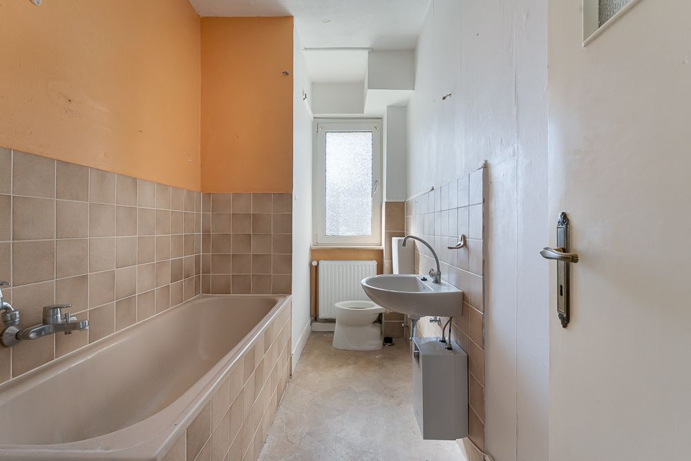 Ein Badezimmer mit Badewanne, Waschbecken, Toilette und Fenster, Wände teils orange und beige gefliest.