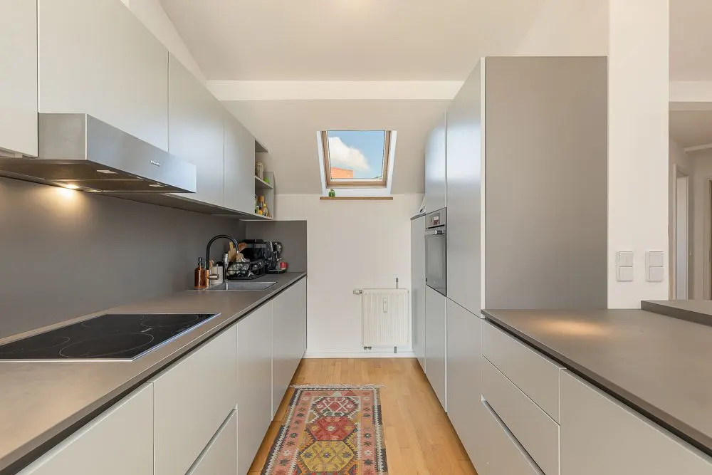 Moderne Küche mit hellen Schränken, Elektroherd, Teppichläufer und Dachfenster.