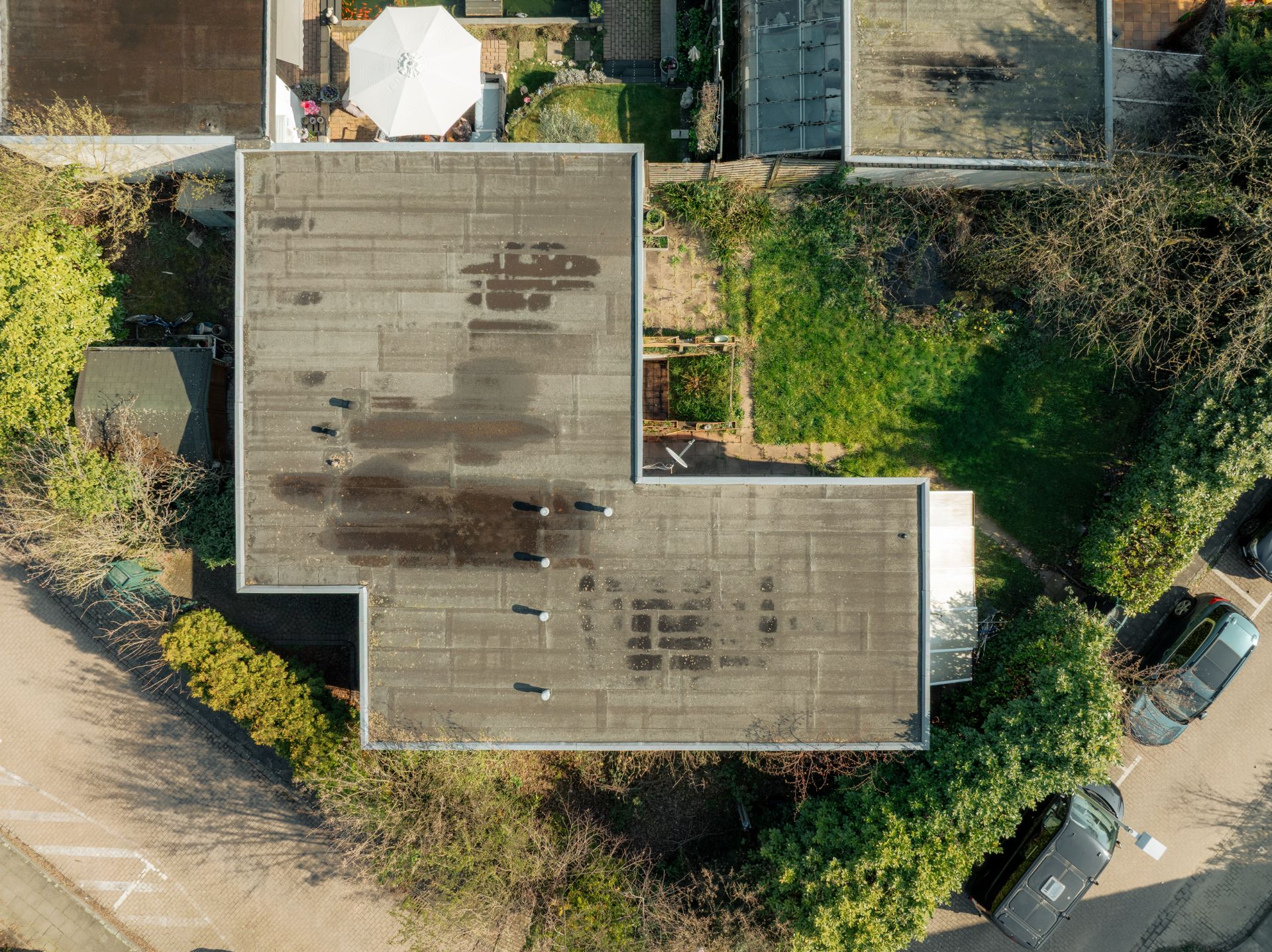 Luftaufnahme eines Flachdachhauses mit Garten und angrenzender Einfahrt.