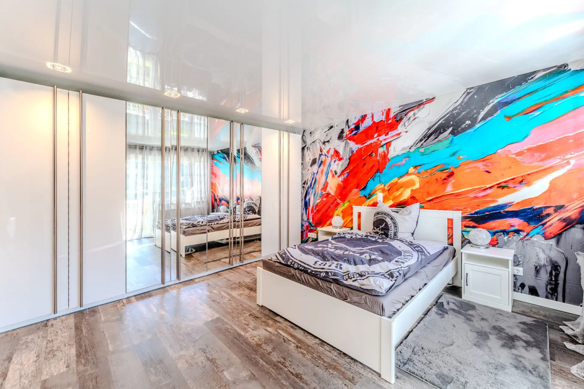 Modernes Schlafzimmer mit großem Spiegelkleiderschrank und bunter Wandmalerei hinter dem Bett.
