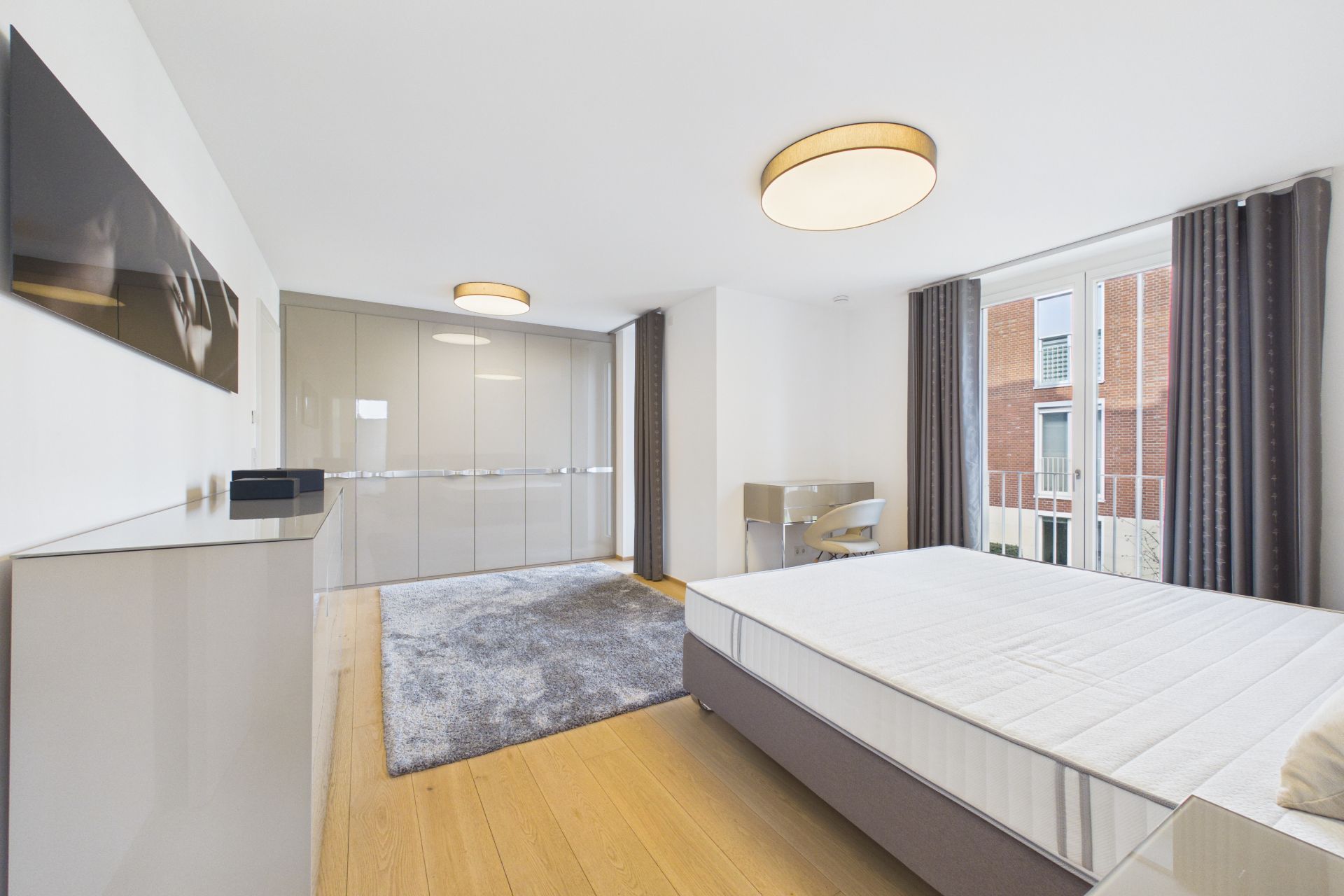 Helles Schlafzimmer mit großem Bett, Teppich, Schreibtisch, Einbauschrank und Fenster.