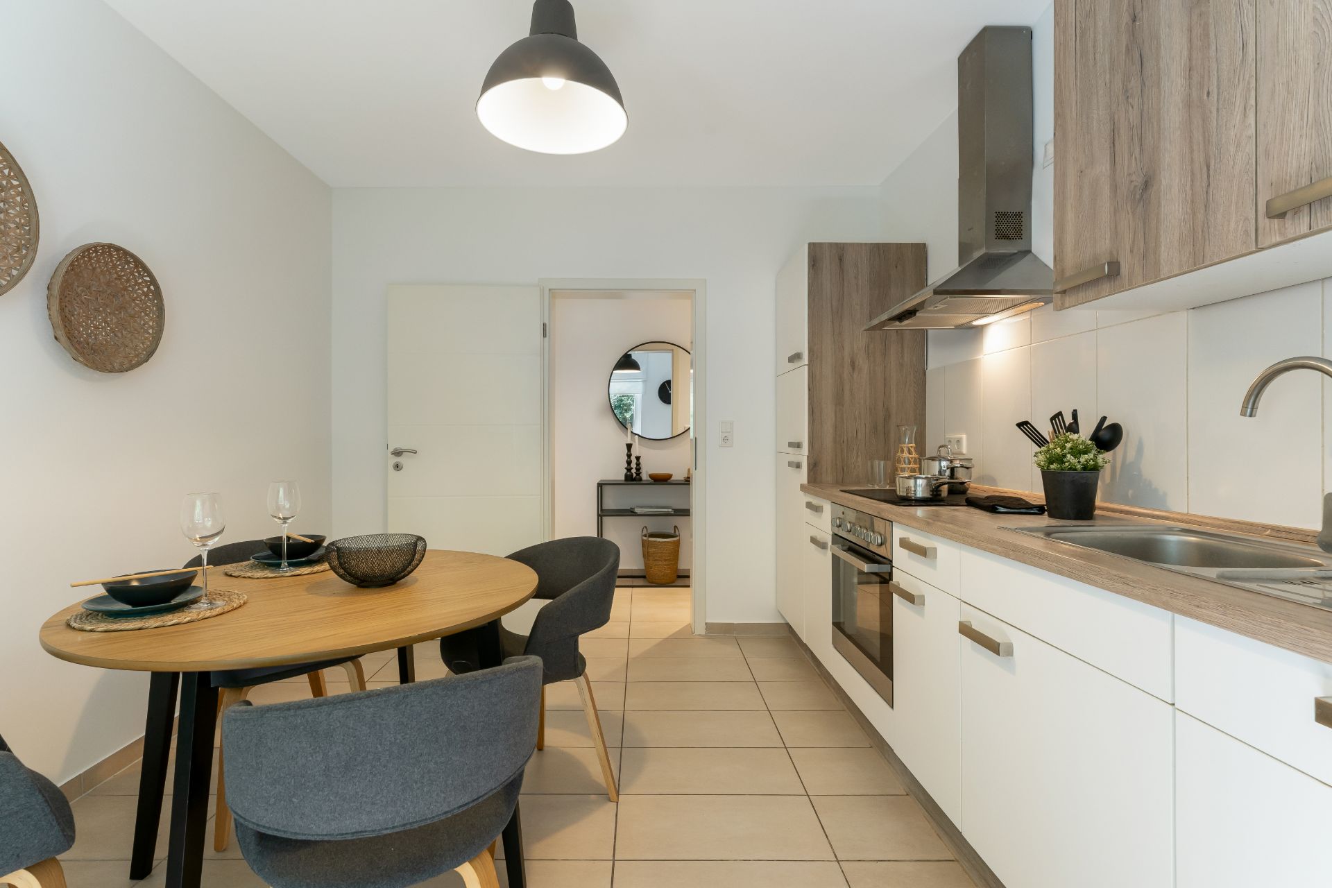 Moderne Küche mit Essbereich, Holzmöbeln, runden Tisch und vier Stühlen, helle Fliesen.