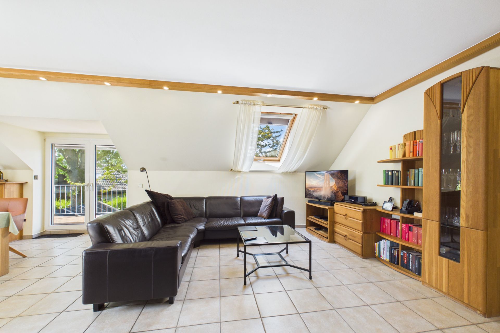 Wohnzimmer mit schwarzem Ecksofa, Glastisch, Schrankwand, Fernseher und Fenster im Dachgeschoss.