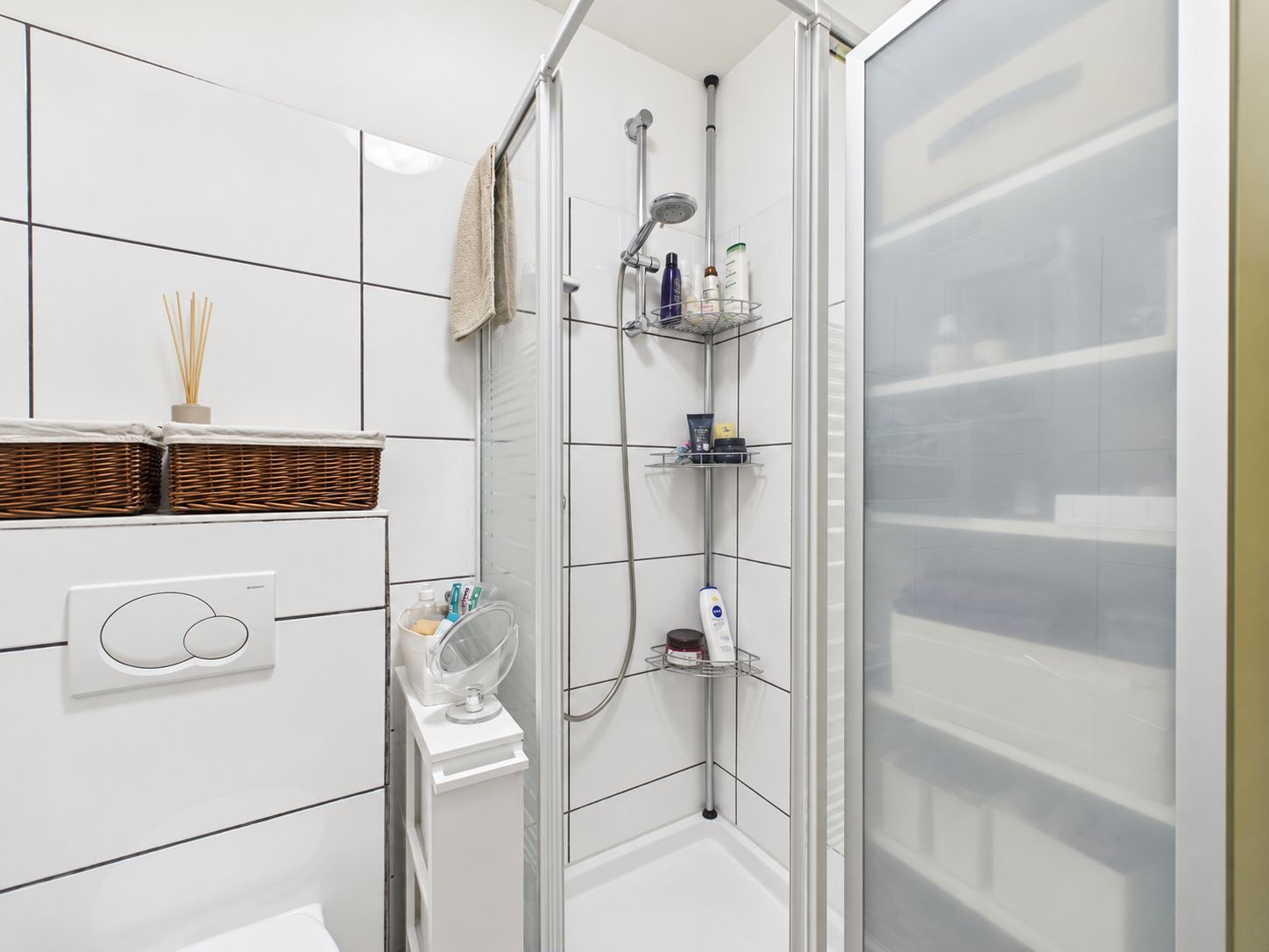 Kleines Badezimmer mit Dusche, Toilette, Regal und gefliesten Wänden.