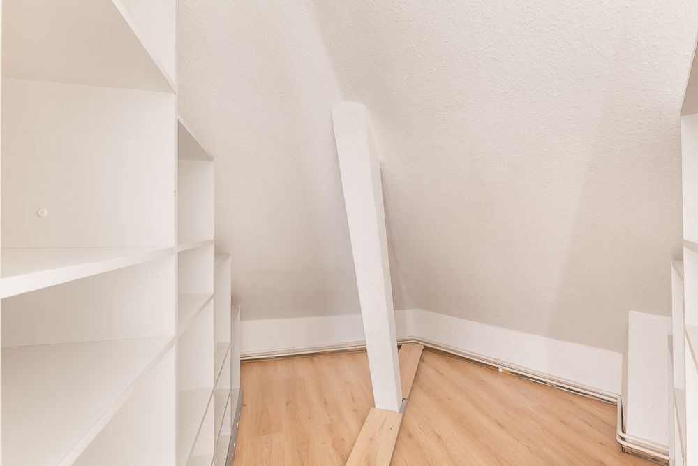 Weißer Einbauschrank unter einer Dachschräge mit hellem Holzfußboden.