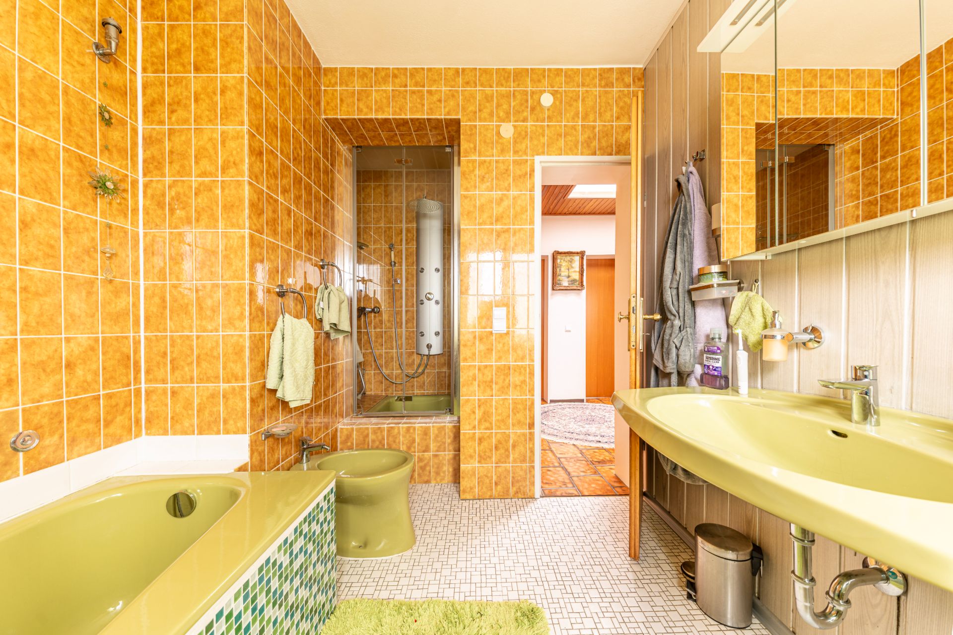 Badezimmer mit gelber Badewanne, Bidet, Doppelwaschbecken und orange gefliesten Wänden.
