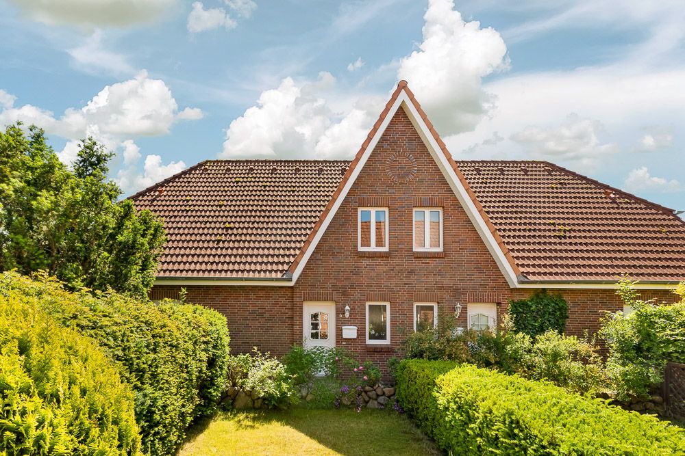 Backstein-Wohnhaus mit Spitzdach, kleinem Garten und Hecken im Vordergrund.