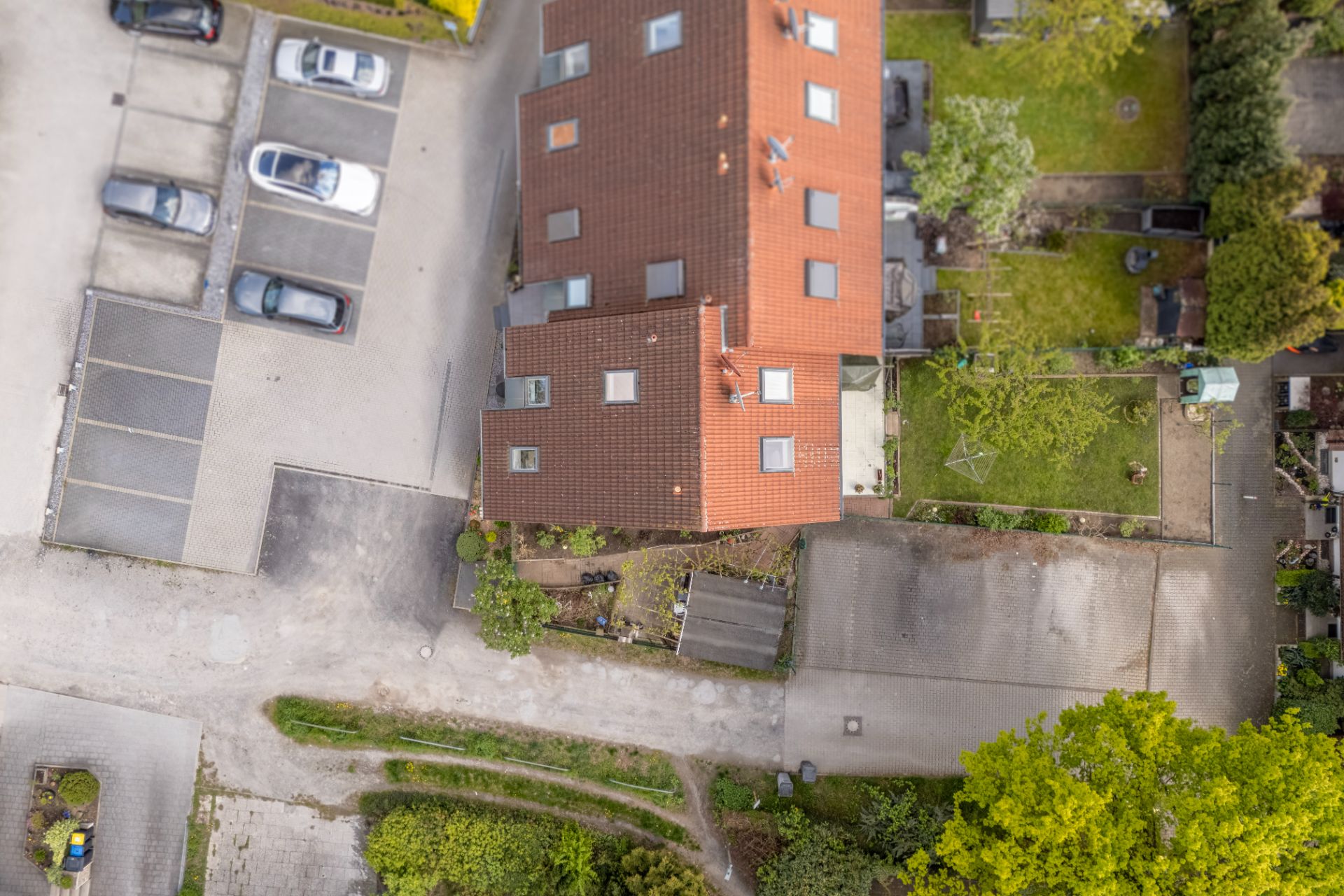 Luftaufnahme eines Wohnhauses mit roten Dachziegeln, Parkplätzen und angrenzenden Gärten.