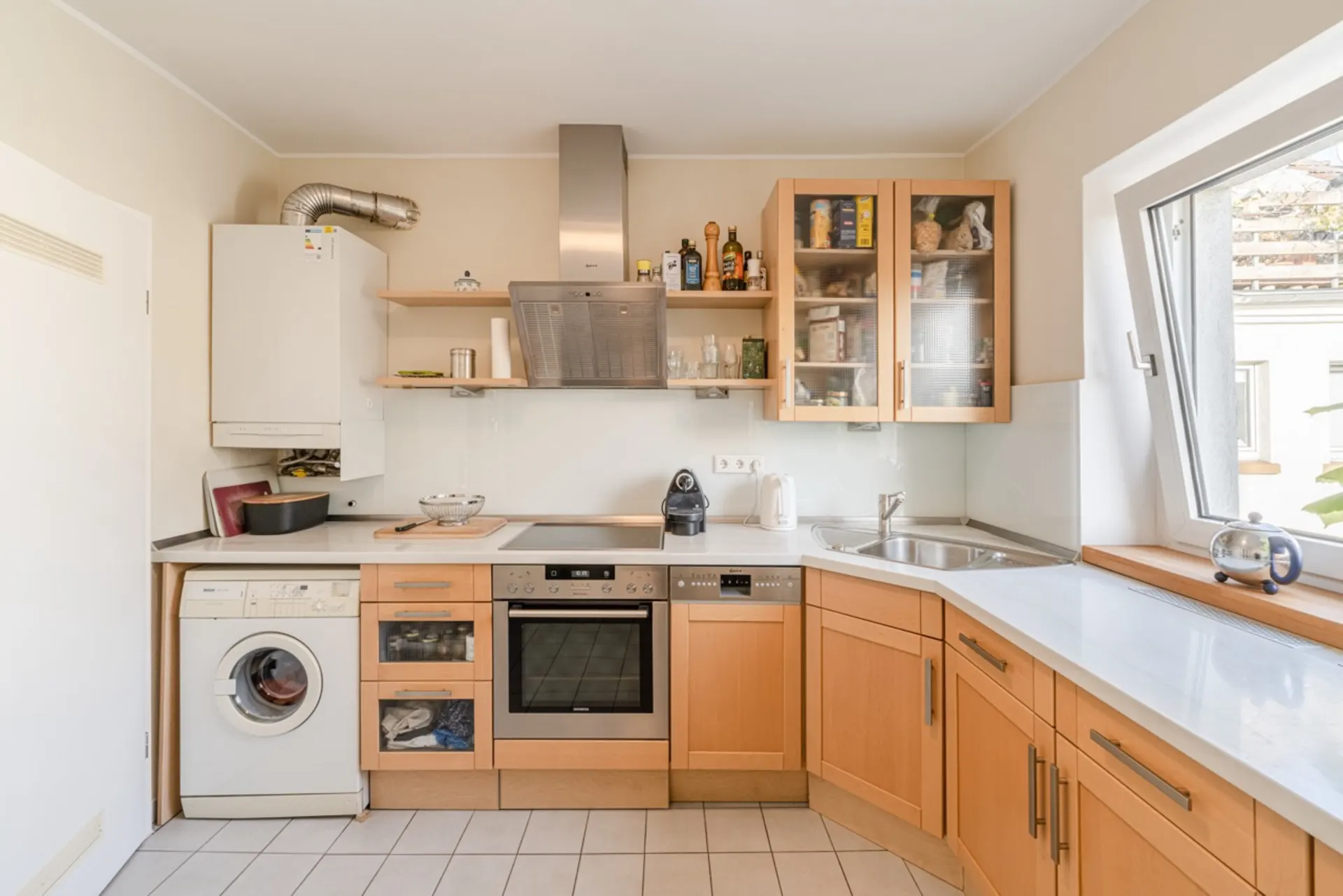 Helle Küche mit Holzschränken, Herd, Waschmaschine, Spüle und großem Fenster.