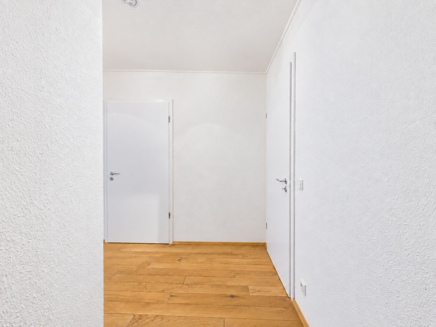 Heller Flur mit weiß gestrichenen Wänden, Holzboden und zwei weißen Türen.