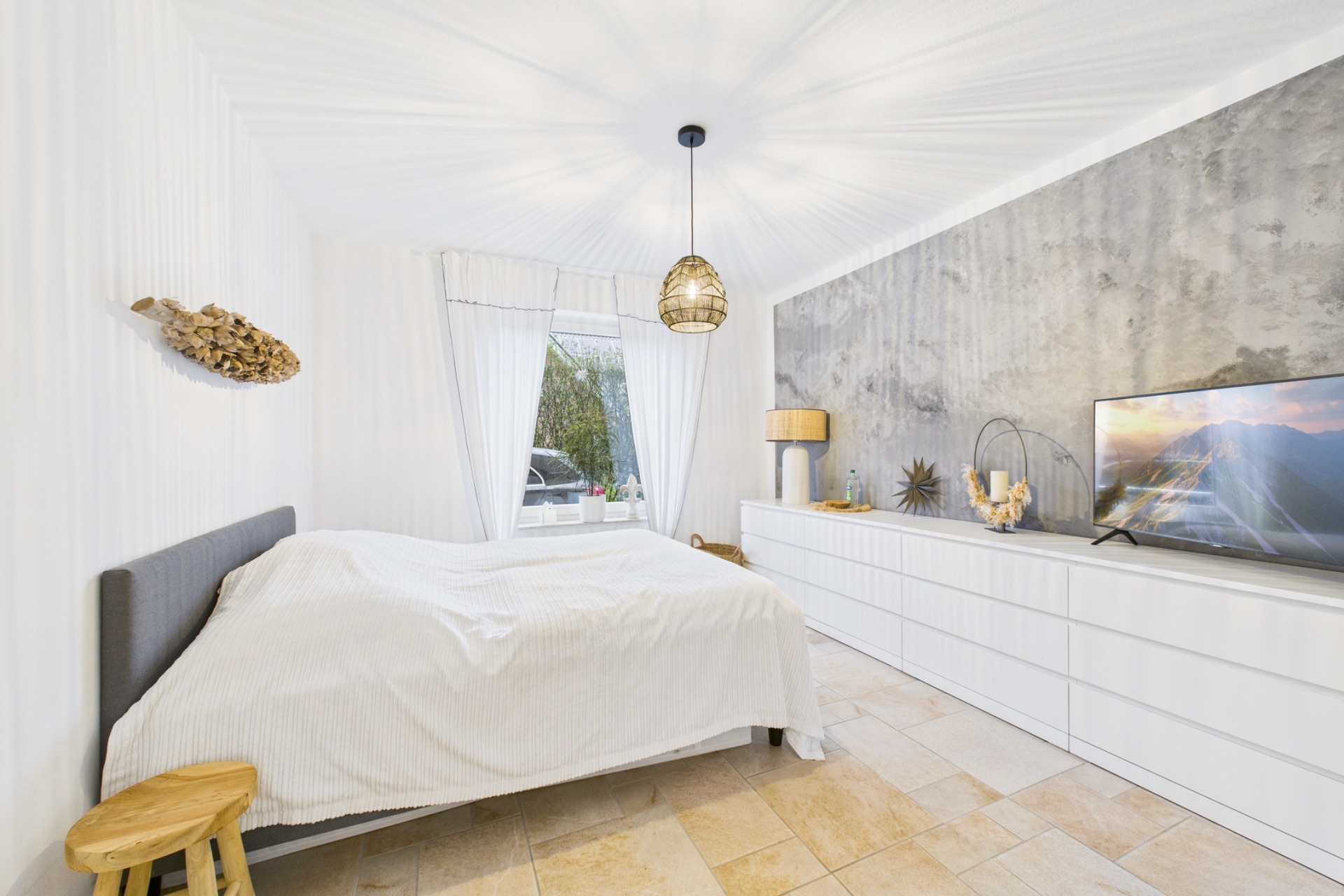 Helles Schlafzimmer mit Doppelbett, großem Fenster, langer Kommode und Fernseher.