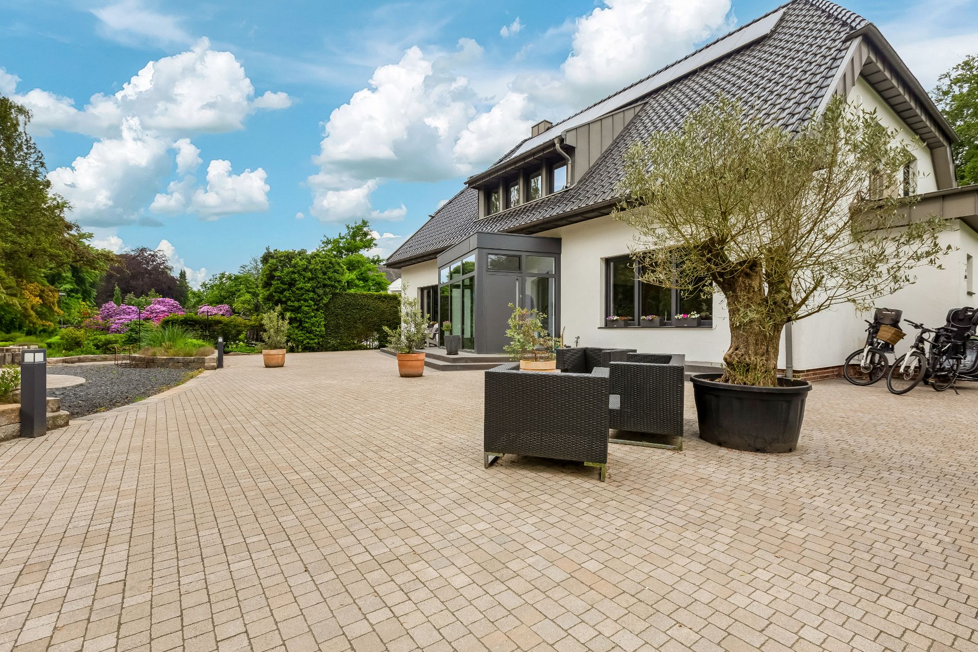 Große Terrasse mit Gartenmöbeln, Pflanzkübeln und einigen Fahrrädern vor einem Einfamilienhaus.