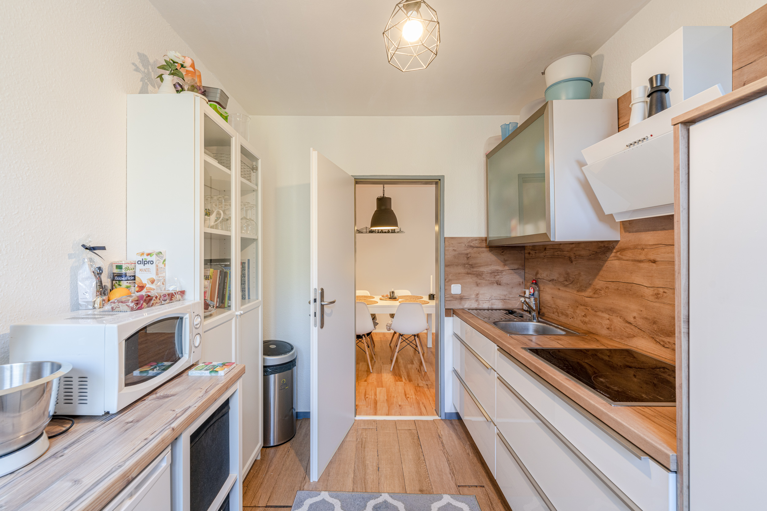 Helle Küche mit Holzarbeitsplatte, Mikrowelle und Blick ins Esszimmer mit weißen Stühlen.