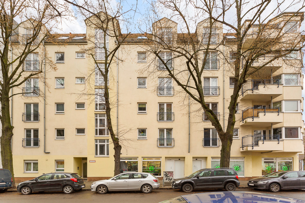 Mehrstöckiges Wohnhaus mit Balkonen und parkenden Autos davor.