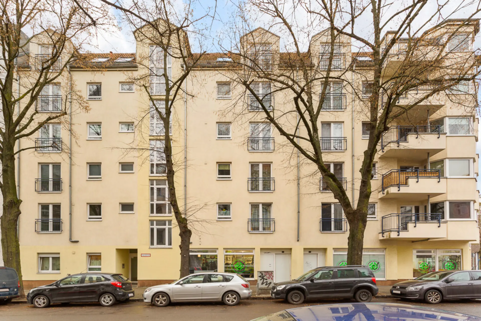 Mehrstöckiges Wohnhaus mit Balkonen und parkenden Autos davor.
