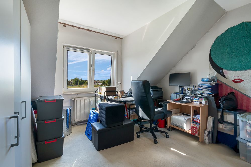 Helles Arbeitszimmer mit Schreibtisch, Stuhl, Computer und Regalen unter Dachschräge.