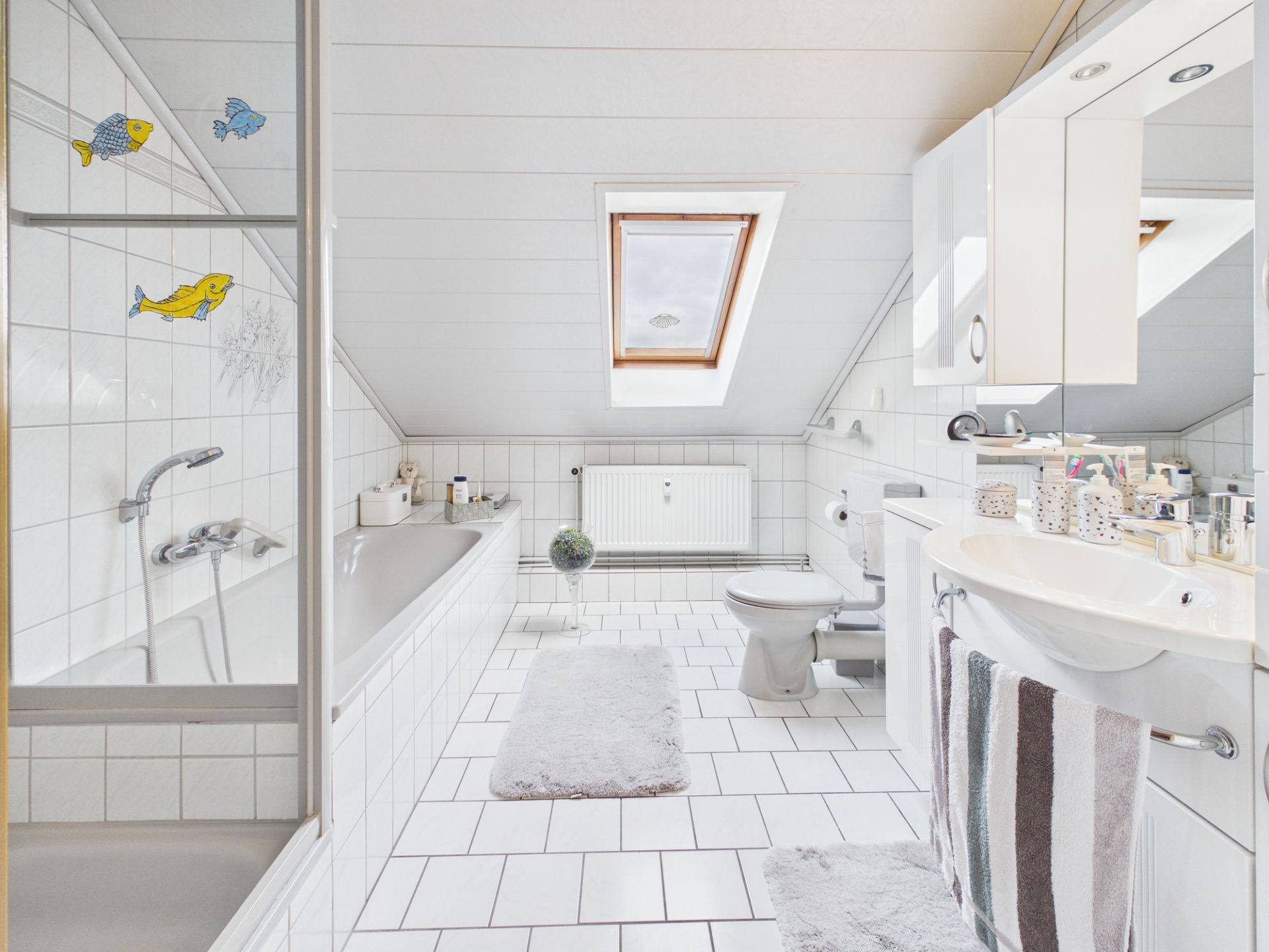 Helles Badezimmer mit Badewanne, Waschbecken, WC, Dachfenster und weißen Fliesen.