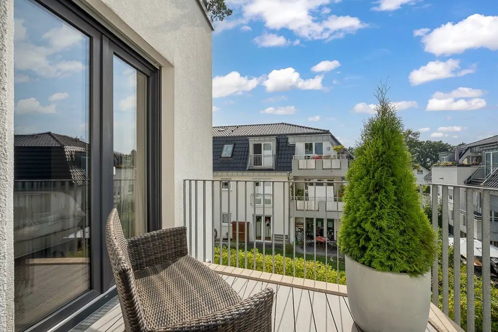 Balkon mit Stuhl, Pflanze im Topf und Blick auf benachbarte Wohnhäuser bei sonnigem Wetter.