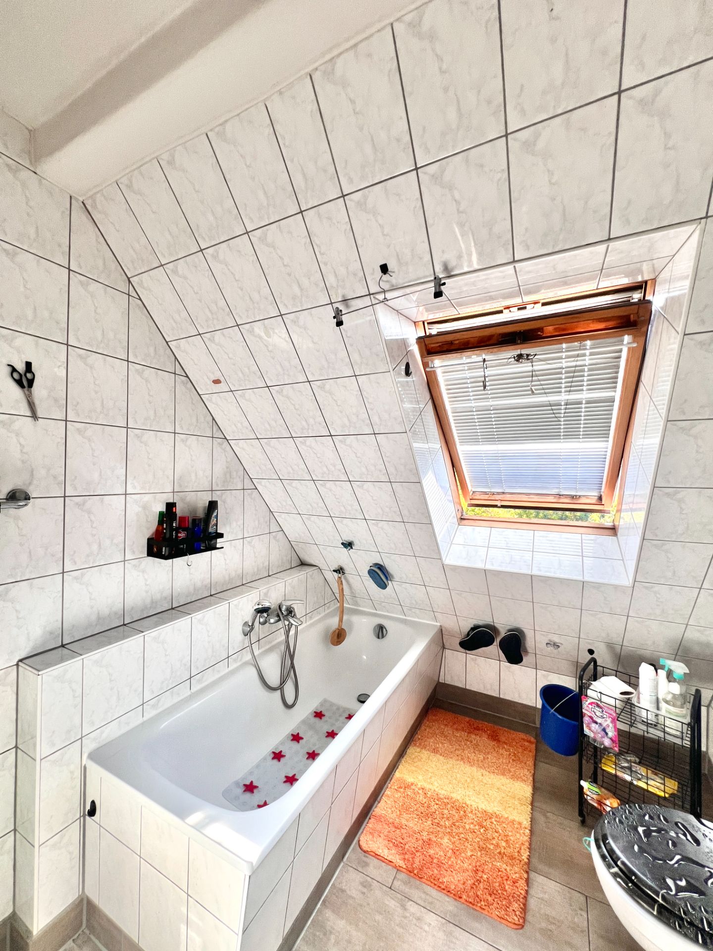Helles Badezimmer mit Badewanne, Dachfenster und oranger Badematte.